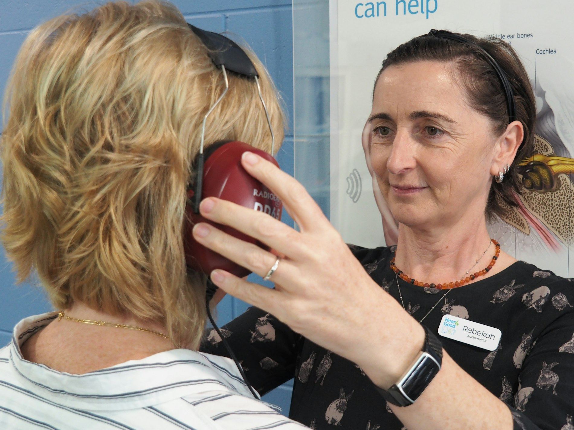 An audiologist conducts a hearing test on a woman using headphones in a clinic.