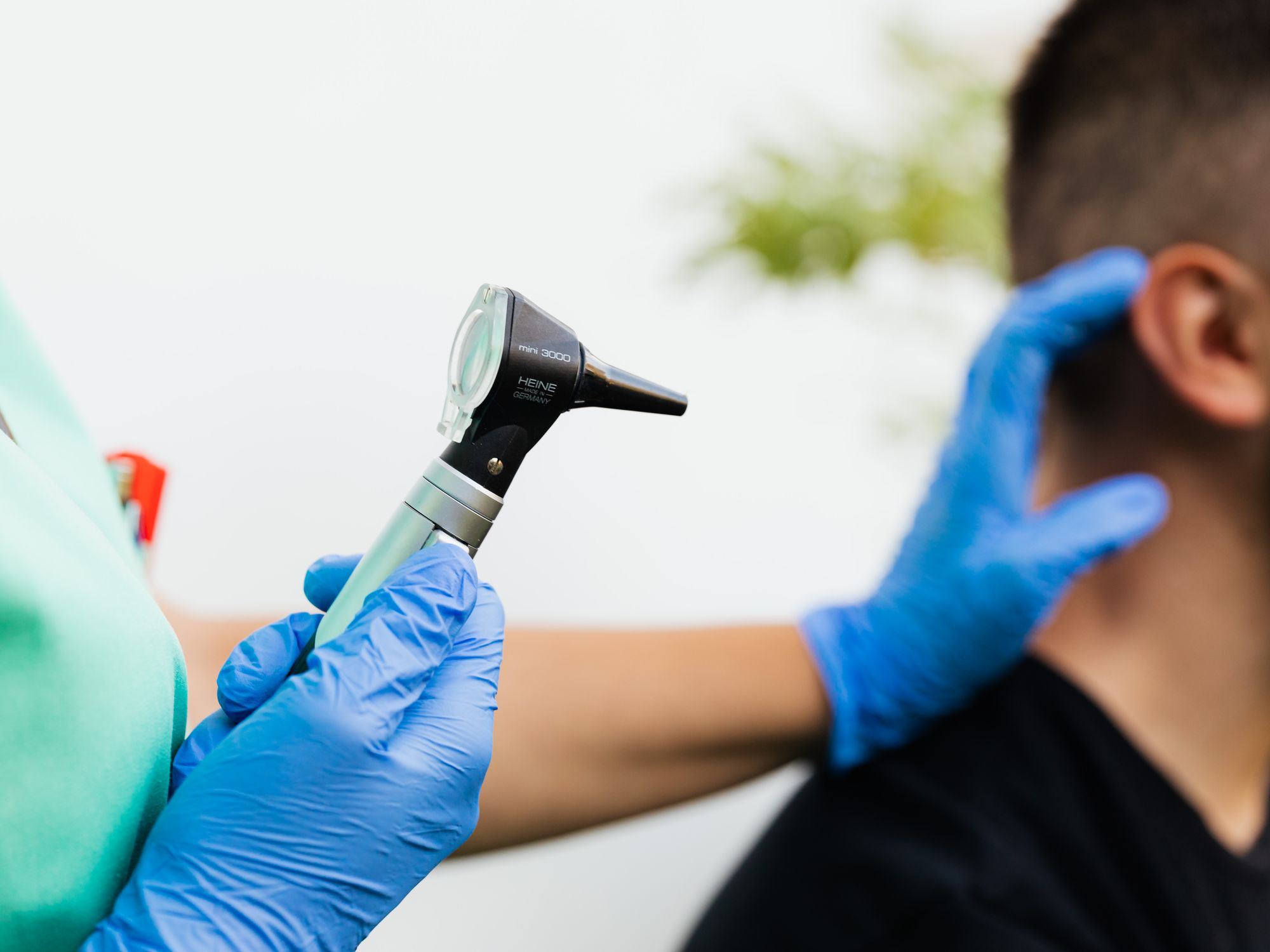 A gloved clinician examines a patient's ear with an otoscope.