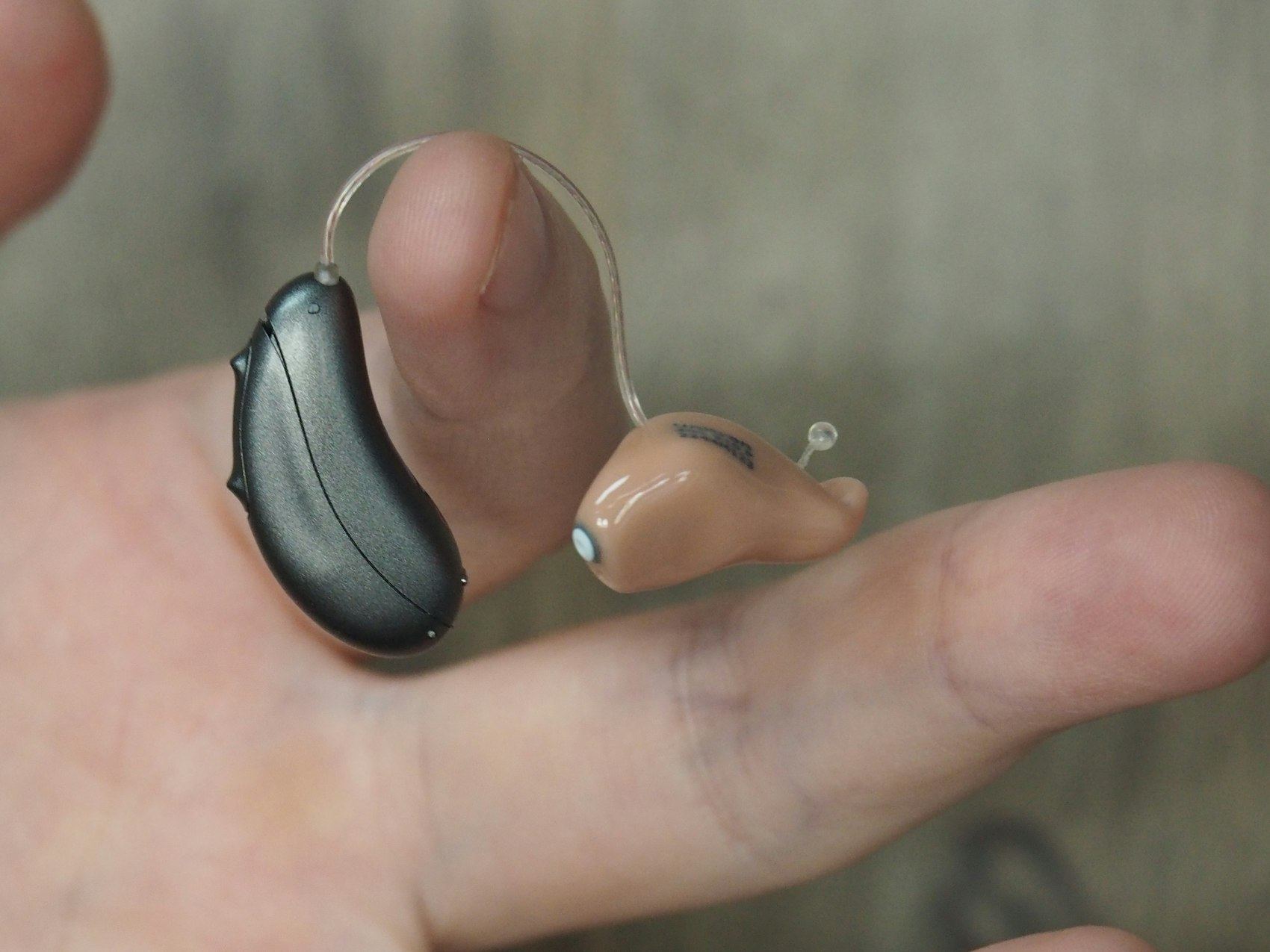 Close-up of two hearing aids resting on a fingertip.