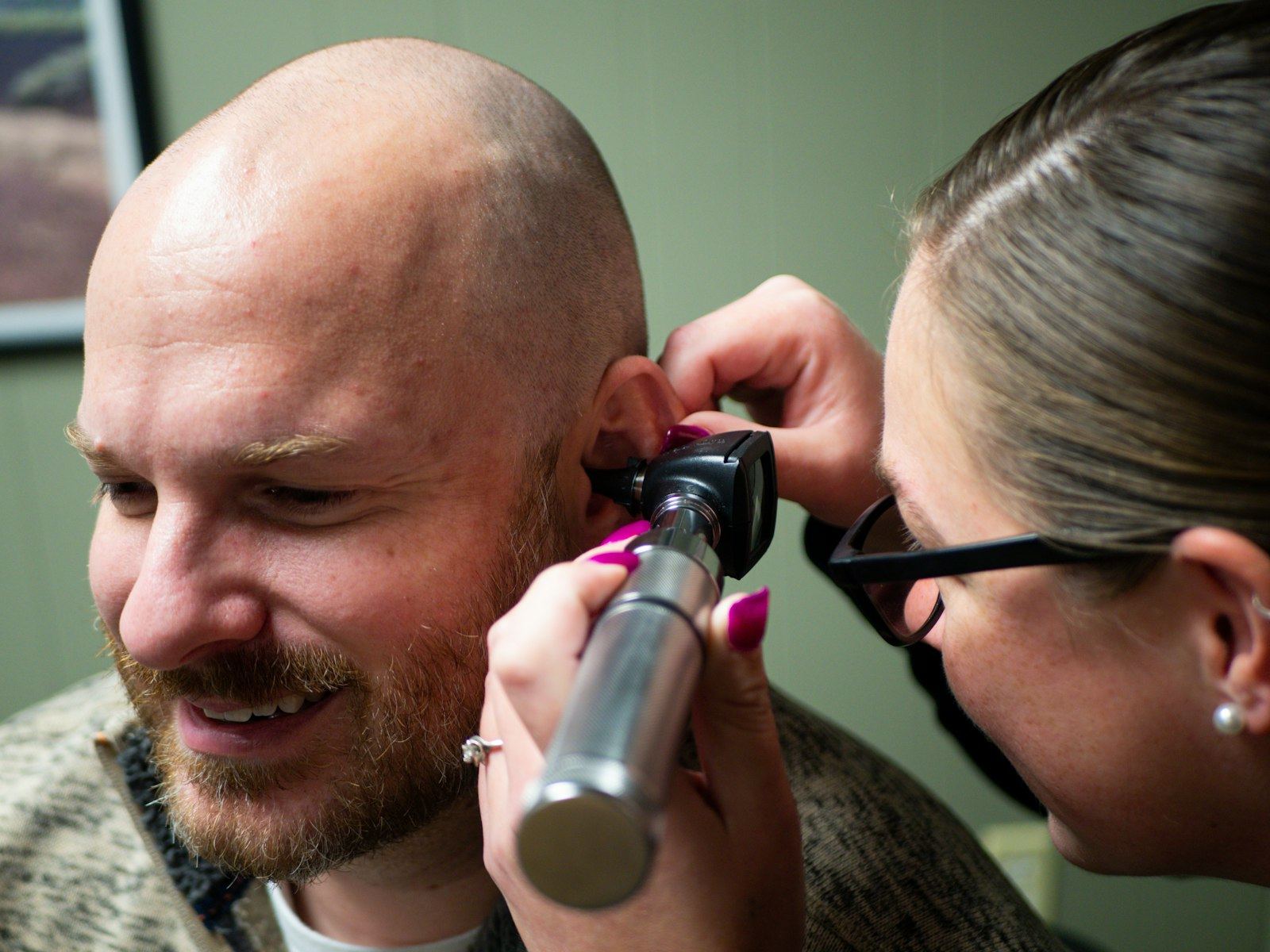 Clinician examines a man's ear with an otoscope in a clinic room.